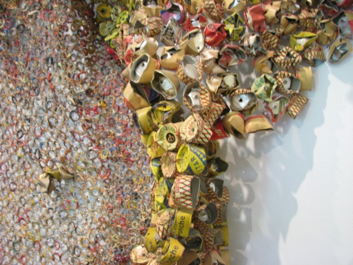 A obra, que lembra um trabalho de tapeçaria, é composta de milhares de tampas de alumínio e selos de bebidas alcoólicas.